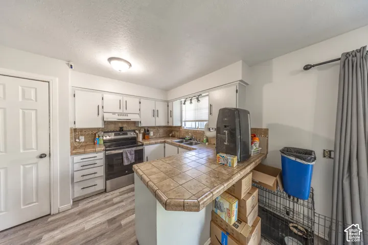 White cabinetry, tile countertops, stainless steel range, and wood-finish flooring