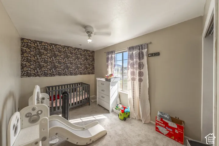 Bedroom featuring neutral-toned carpeting, a decorative accent wall, a single window, and a ceiling-mounted light fixture with an integrated fan