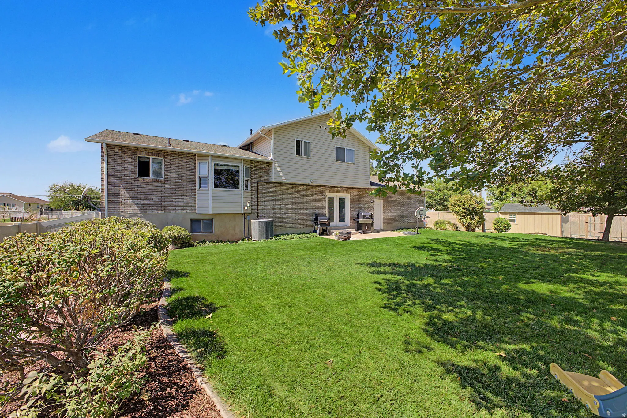 Expansive backyard featuring a lush lawn, a paved patio, and a storage shed