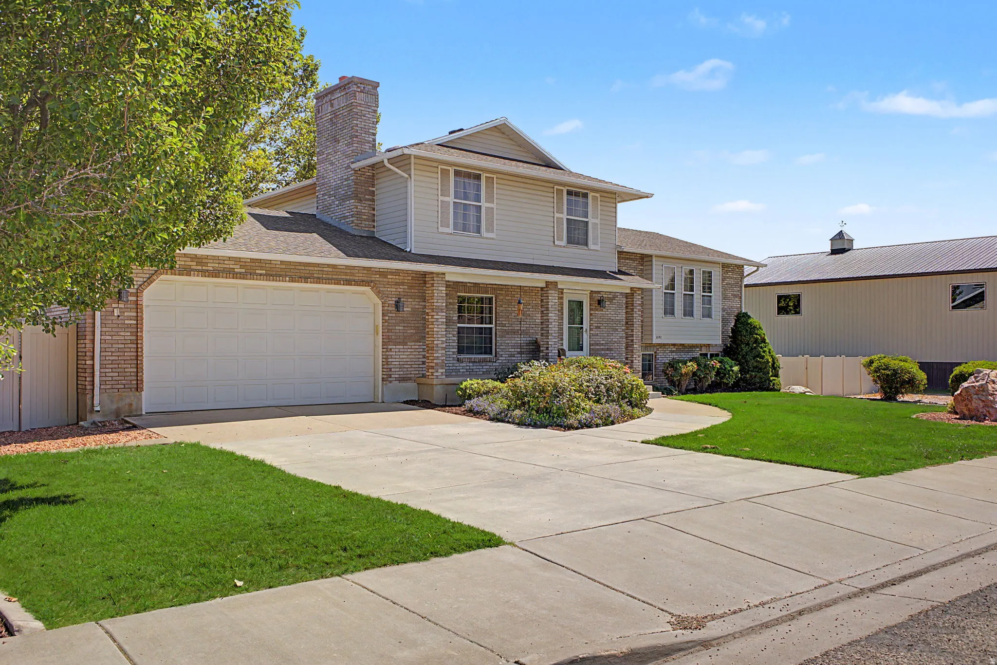 Brick facade and siding exterior featuring a two-car garage, concrete driveway, and established landscaping