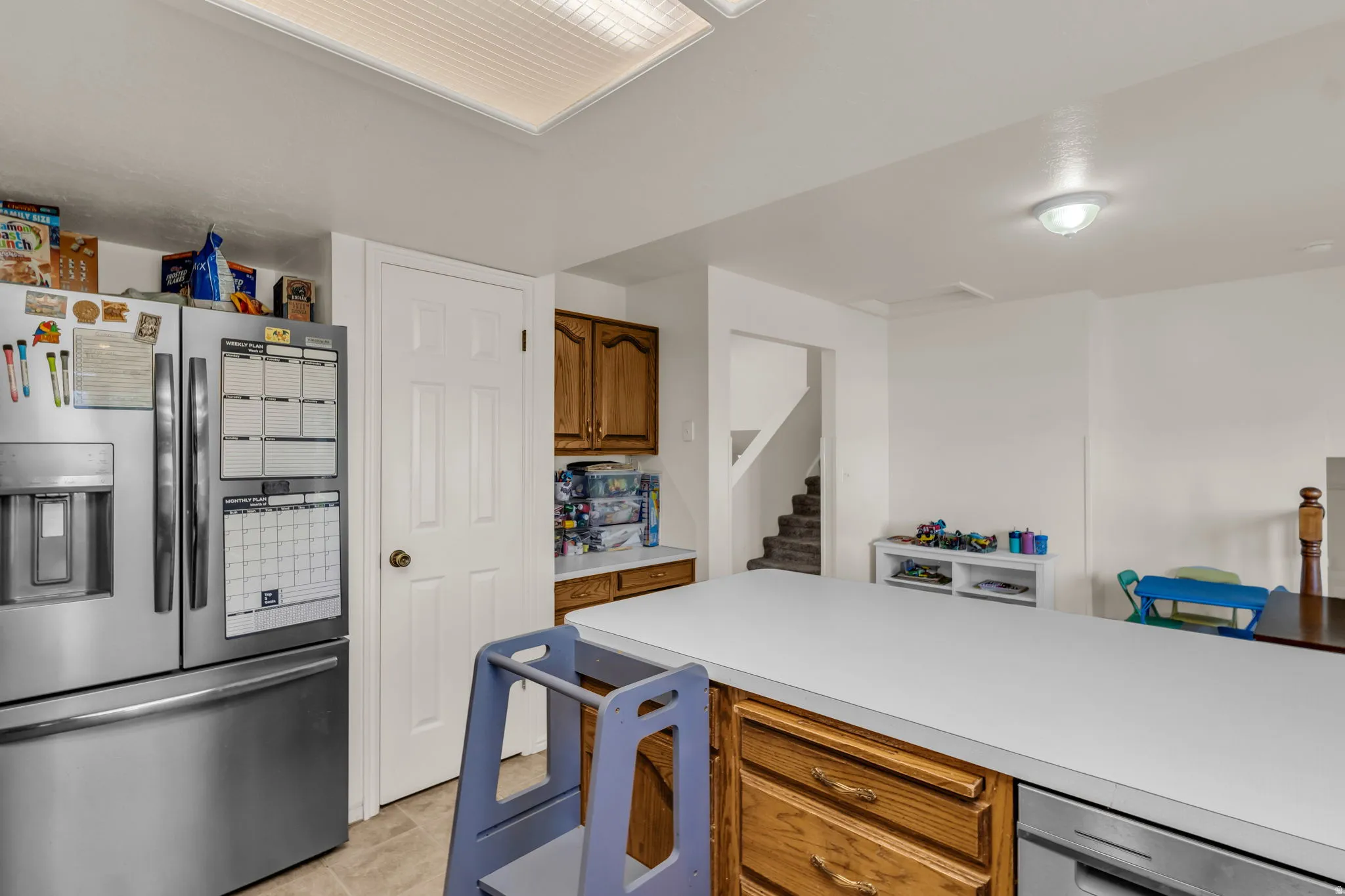 Recessed ceiling light panel, white countertops, wood-finish cabinetry, stainless steel refrigerator, and built-in dishwasher