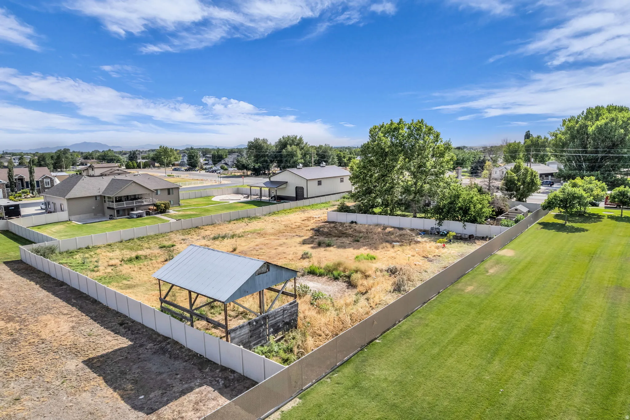 Expansive lot featuring a white perimeter fence, a metal-roofed structure, and a clear blue sky overhead