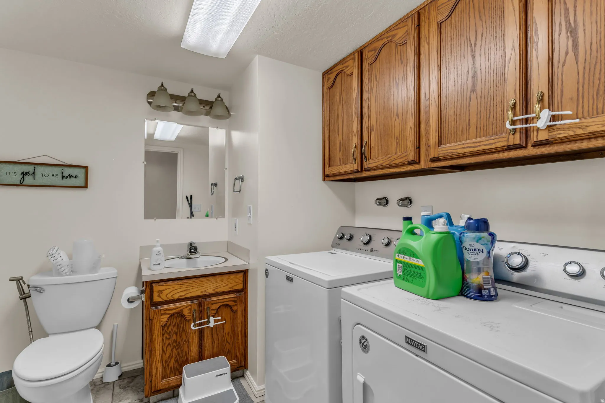 Utility room featuring white front-load washer and dryer with wood-finish cabinetry above, ceramic tile flooring, and abundant storage with wood-finish upper cabinets