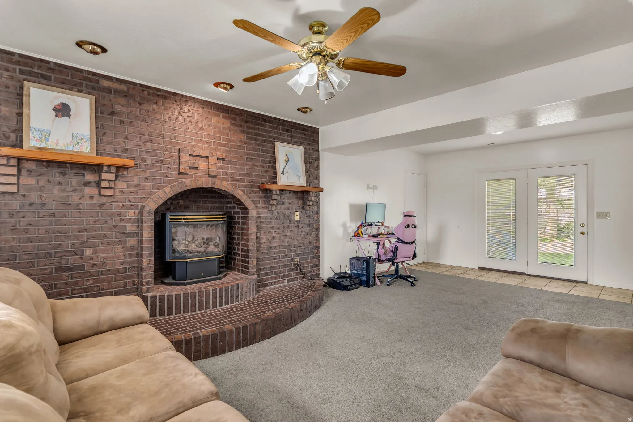 Brick fireplace with an arched opening and integrated hearth seating, ceiling fan with light fixture, recessed ceiling lighting, and double glass-panel doors