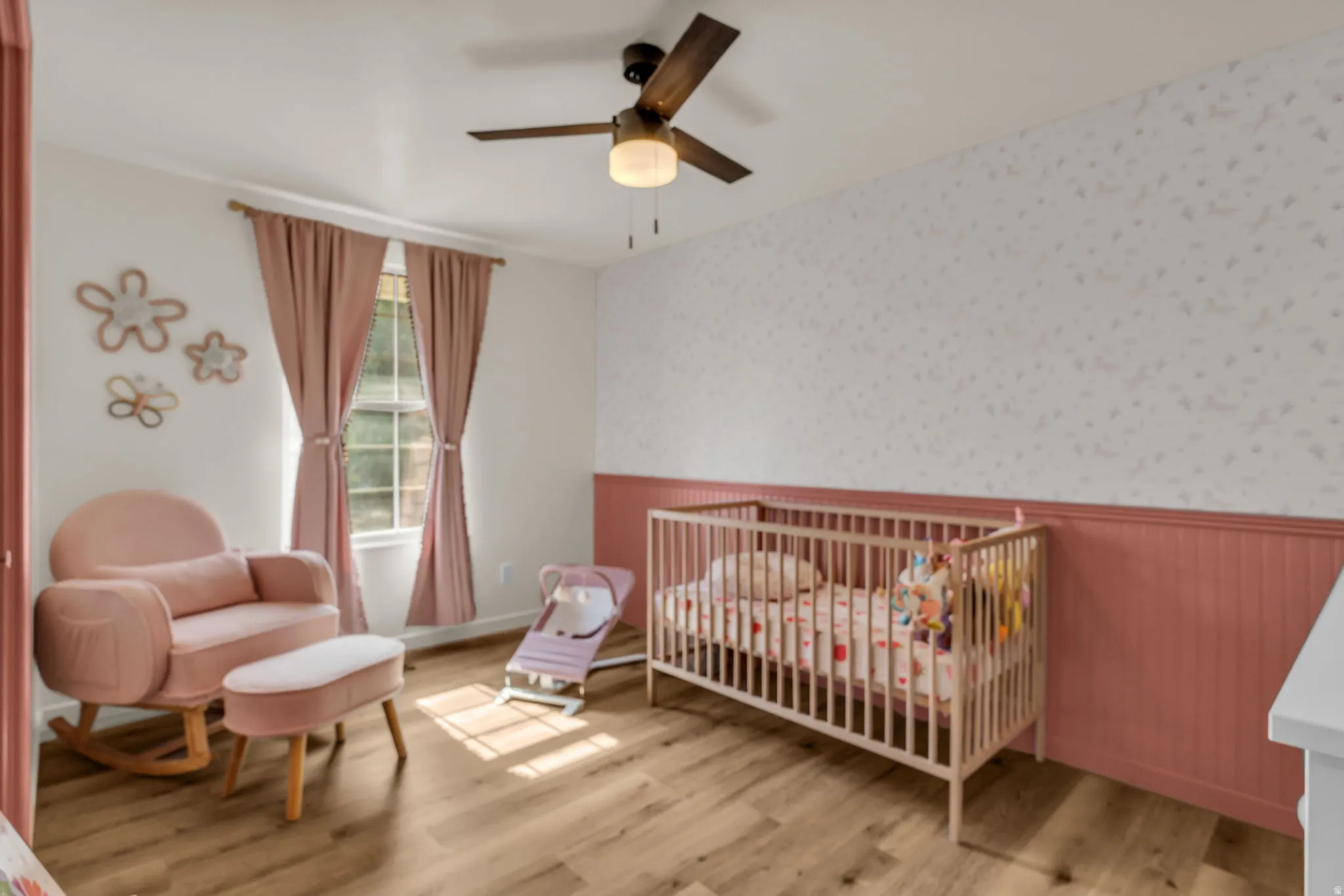 Wood-finish flooring, ceiling fan with integrated lighting, window with drapes, and a wall featuring beadboard paneling