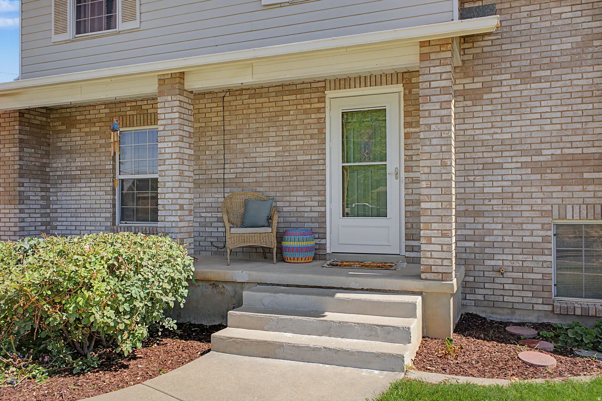 Brick façade home featuring a covered front porch, concrete steps, and a white entry door with a screen