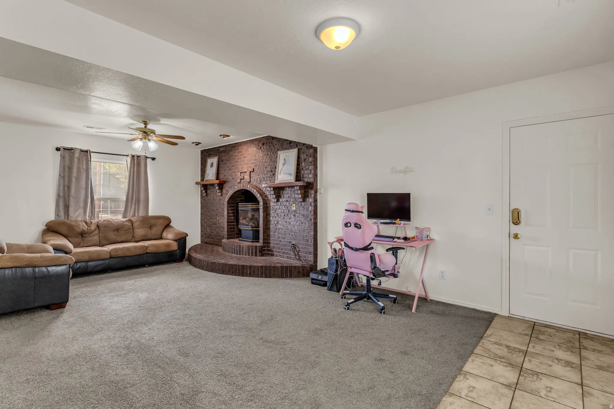 Spacious room featuring a brick fireplace with mantel shelves, a ceiling fan with integrated lighting, and mixed flooring with carpet and tile