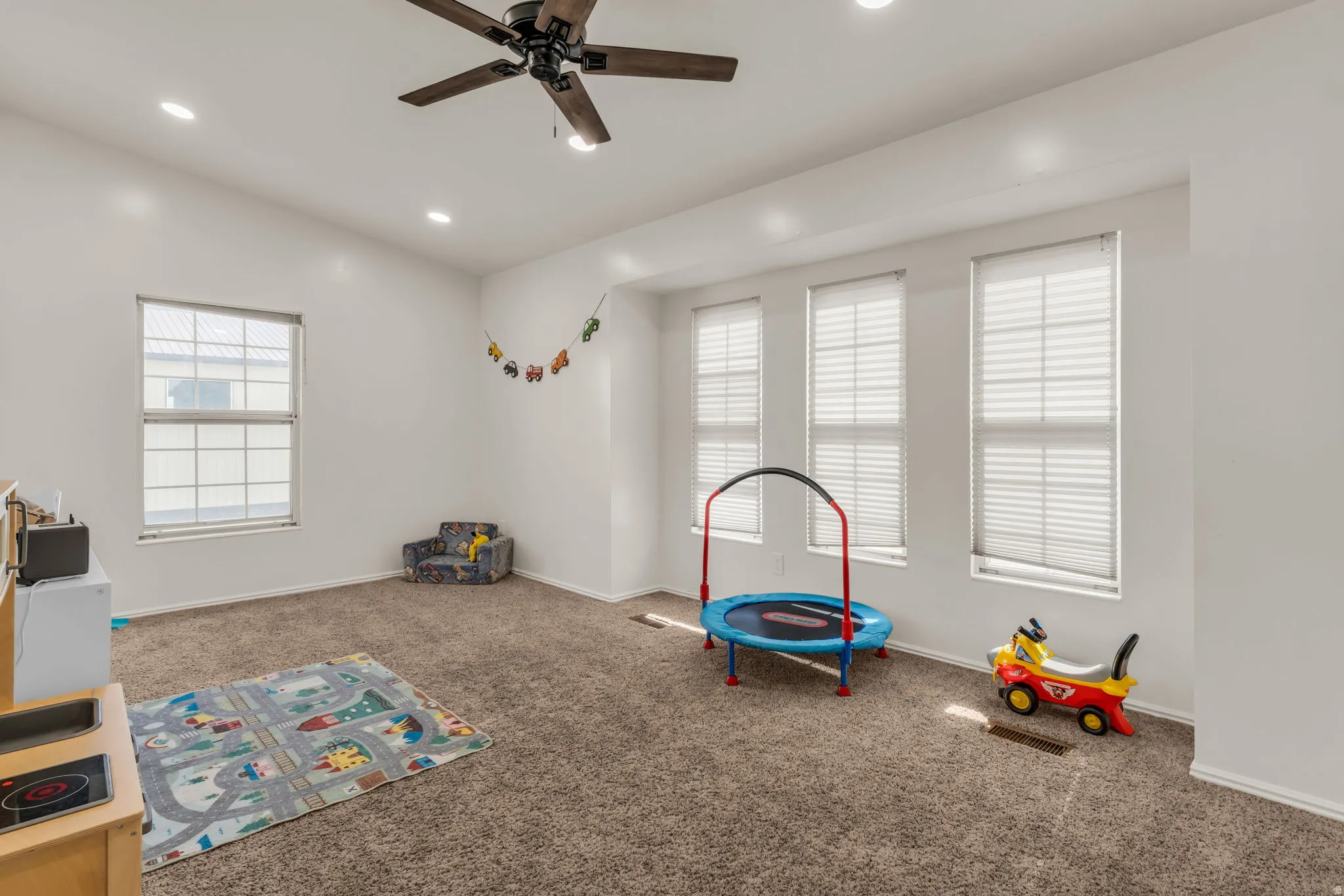 Bright, versatile playroom flooring with carpet throughout and abundant natural light from multiple large windows with plantation shutters
