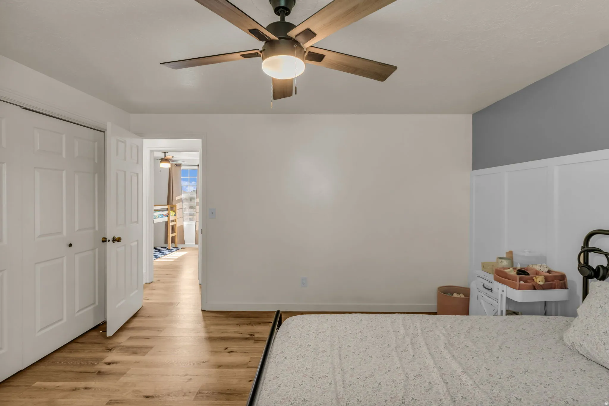 Wood-finish flooring, ceiling fan with integrated lighting, white paneled bifold closet doors, and a board and batten accent wall