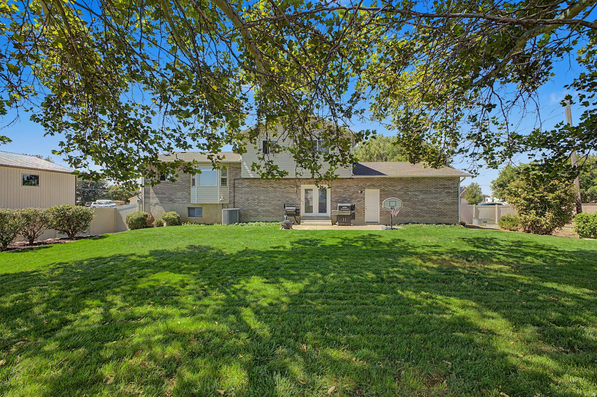 Expansive green lawn with established trees, a paver patio, and French doors
