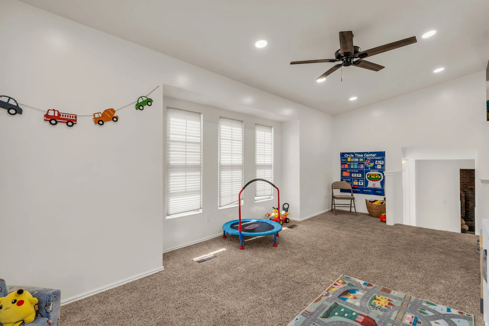 Recessed lighting, ceiling fan, three windows with horizontal blinds, and carpeted flooring