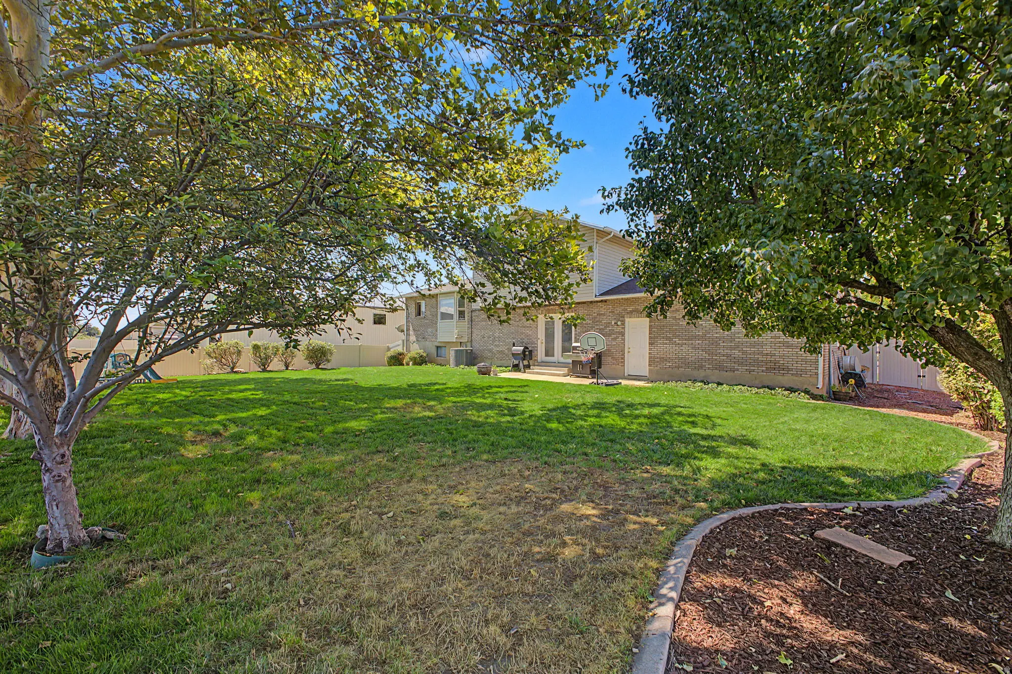 Expansive backyard with a manicured lawn, established trees, and a brick exterior with white trim