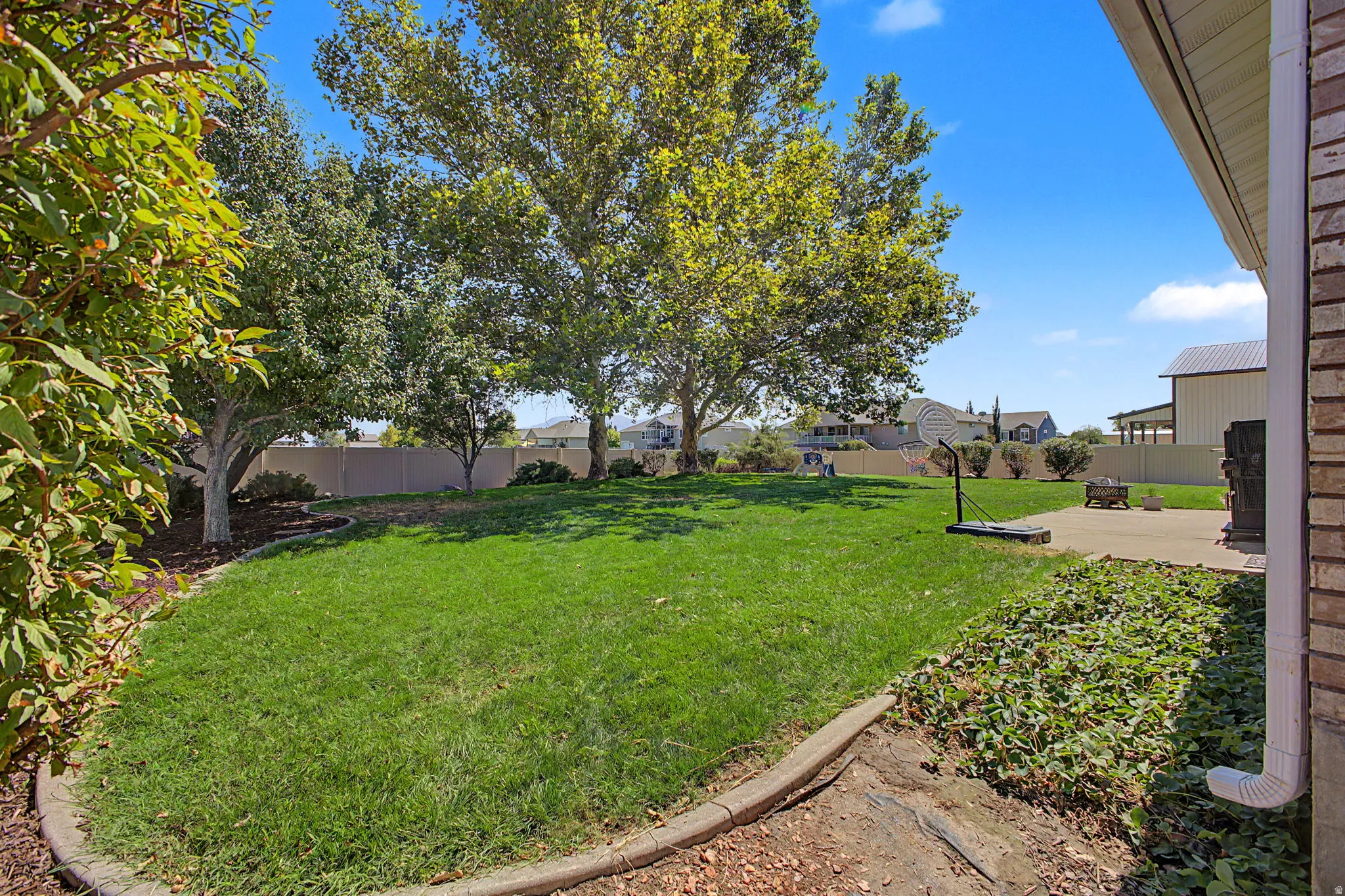 Expansive backyard with a manicured lawn, mature trees, concrete patio, and brick exterior