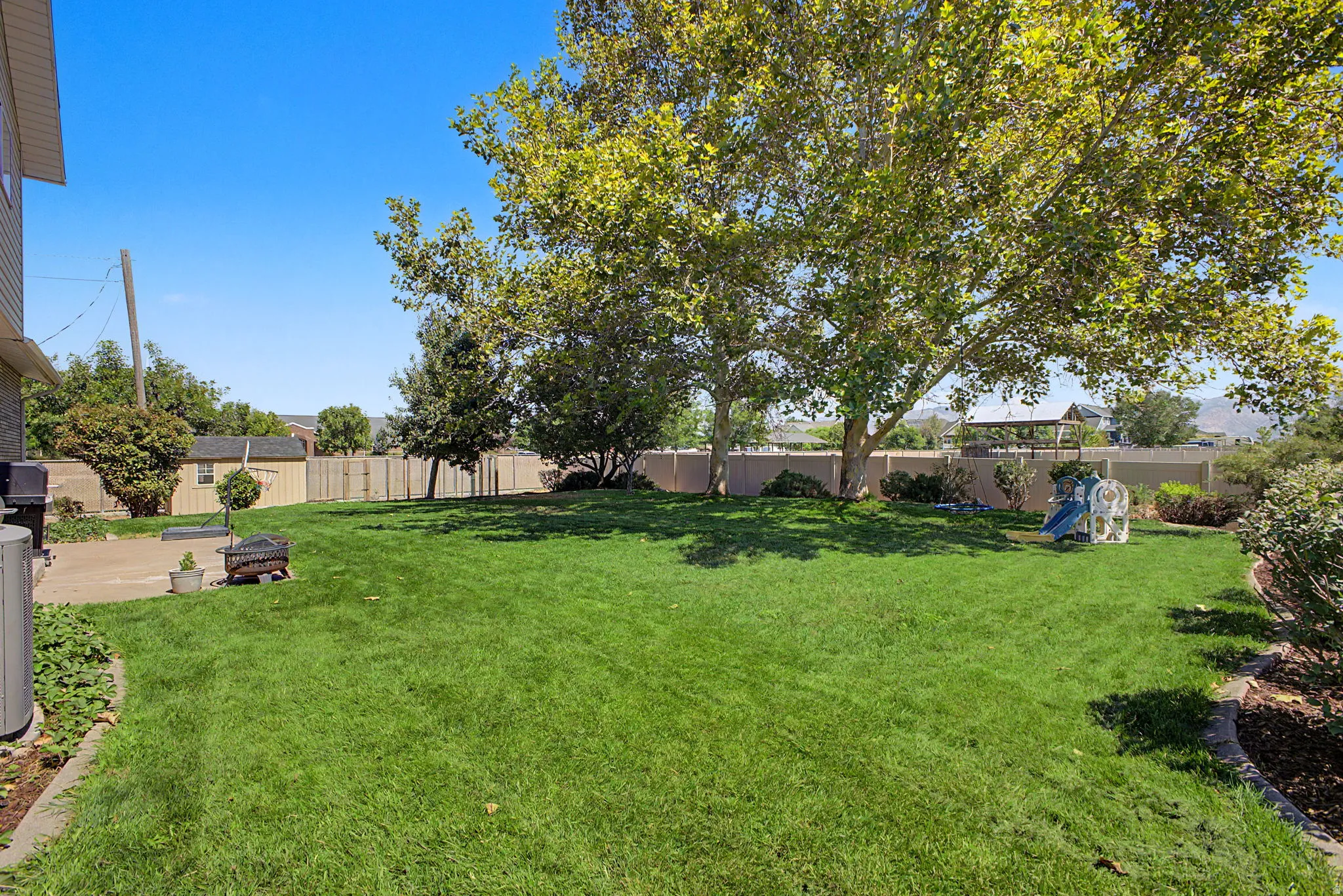 Expansive backyard featuring a manicured lawn, mature trees, and a concrete patio