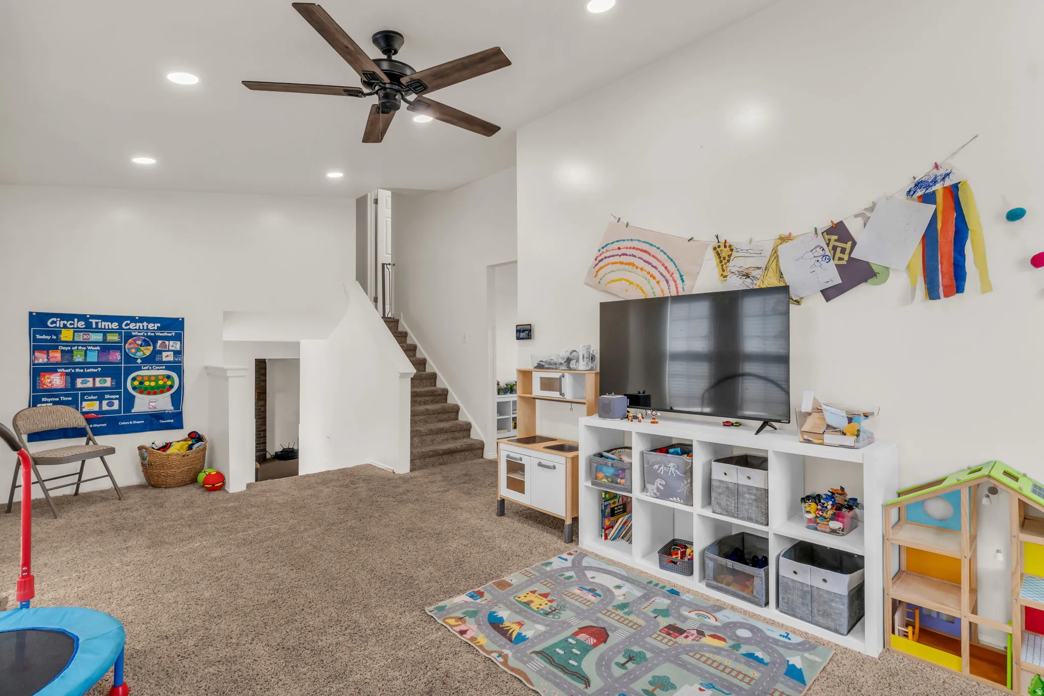 Carpeted room featuring a ceiling fan with wood-finish blades, recessed lighting, and a staircase