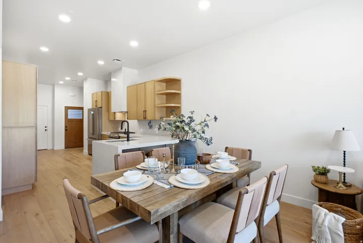 Open-concept living space with light wood-finish flooring, recessed lighting, and a kitchen featuring a center island with a sink, stainless steel appliances, and wood cabinetry