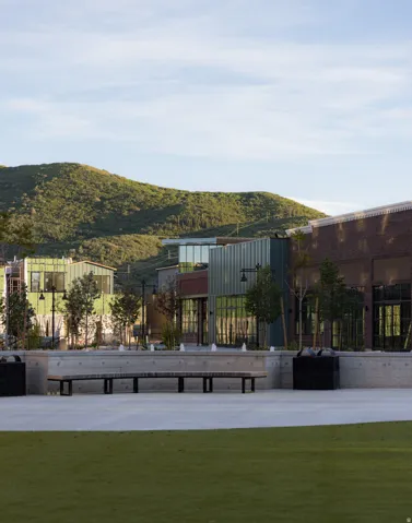 Expansive grassy area with a concrete plaza, built-in concrete seating, water features, and mountain backdrop