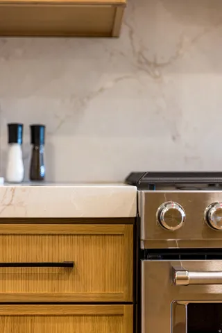 Modern kitchen featuring custom wood-finish cabinetry with integrated hardware, stainless steel dual-fuel range with dual convection ovens, and a light stone-finish countertop with integrated backsplash