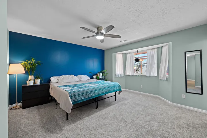 Spacious room featuring a ceiling fan, bay window, and soft gray carpeting