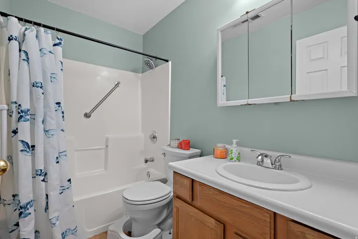 Tub/shower combination with a grab bar, wood-finish vanity with an integrated sink, chrome faucet, and mirrored medicine cabinet