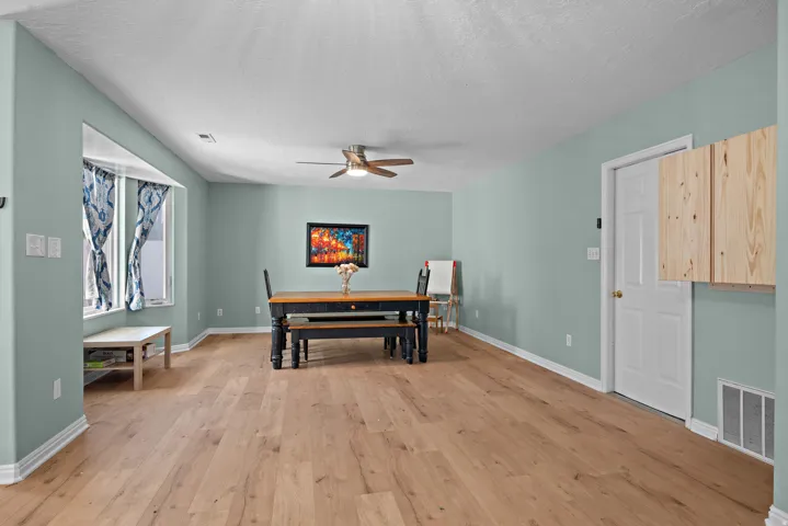 Wood-finish flooring throughout, recessed window alcove, ceiling fan with integrated lighting, and built-in wooden cabinetry