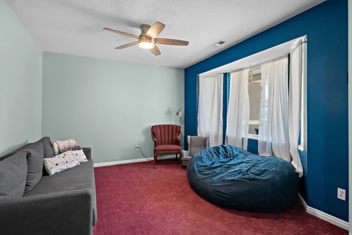 Spacious room featuring a ceiling fan with integrated lighting, a broad bay window, and vibrant wall colors