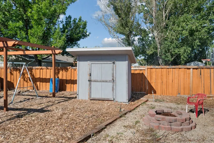 Wood-framed pergola structure, wood plank fencing, utility shed, and a stone fire pit