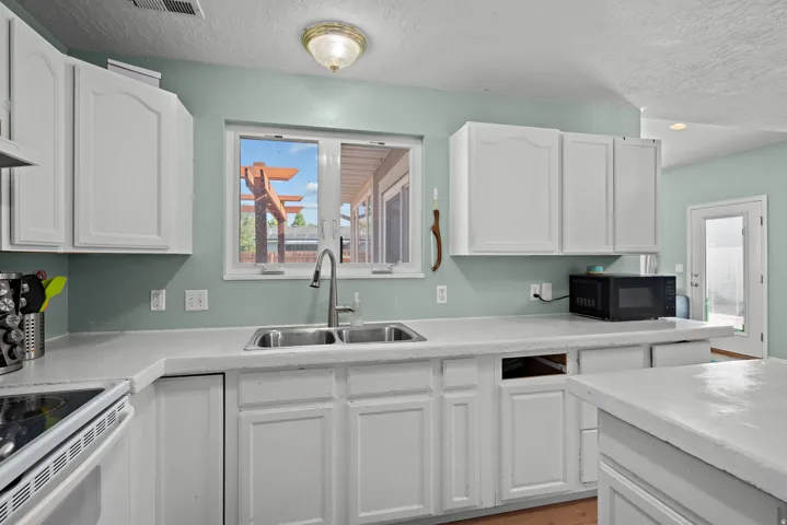 White cabinetry with brushed nickel hardware, stainless steel double basin sink with gooseneck faucet, light-toned countertops, and a window providing natural illumination
