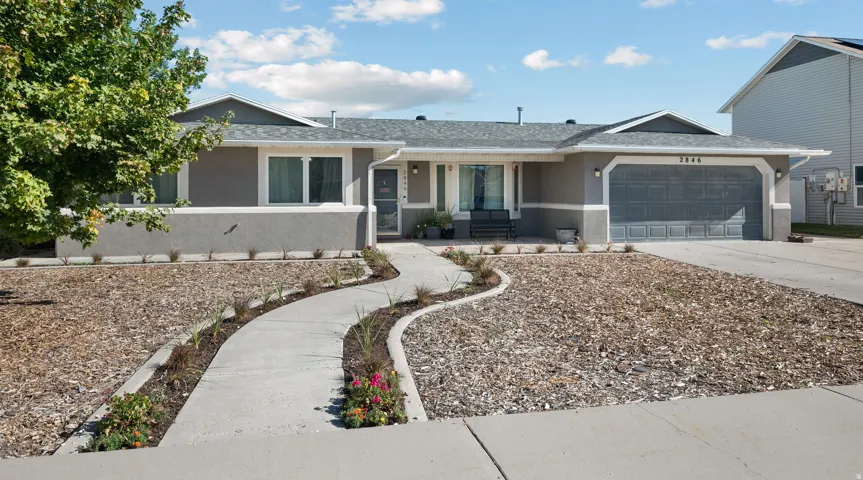 Single-story residence featuring a gray stucco exterior, an attached two-car garage, and a concrete curved pathway