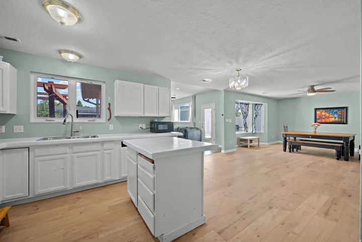 White cabinetry, wood-finish flooring, kitchen island, ceiling fan, and pendant lighting