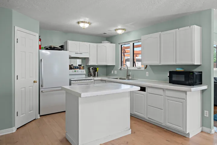 Kitchen featuring white cabinetry, light countertops, wood-finish flooring, a built-in dishwasher, and a window above the sink