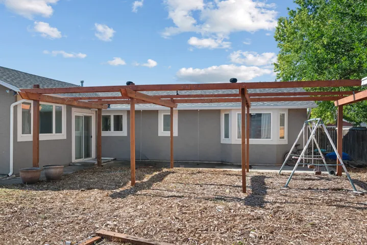 Rear exterior featuring a wooden pergola, sliding glass door, and multiple windows