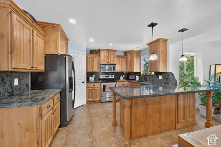 Kitchen featuring wood-finish cabinetry, granite countertops, stainless steel appliances, a center island with pendant lighting, and tiled flooring
