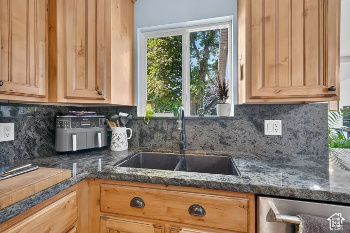 Kitchen featuring wood cabinetry, dark stone countertops, a double basin sink with a gooseneck faucet, and a window