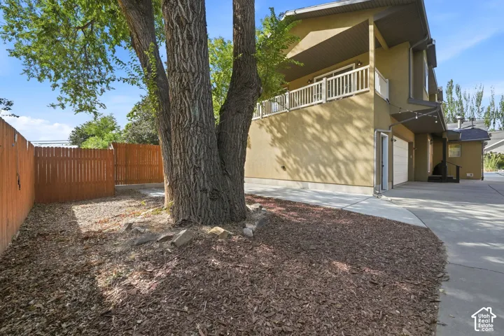 Mature tree with ground cover, wood privacy fencing, stucco exterior, upper-level balcony, and an attached garage
