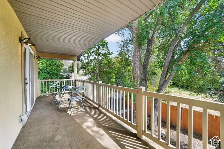 Covered outdoor balcony with a light-colored stucco exterior, sliding glass door, and a white railing