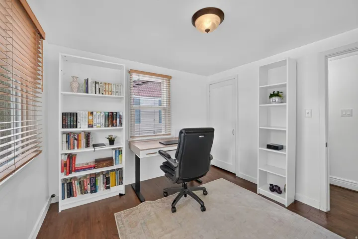 Rich wood-finish flooring, bright white walls, two windows with wood blinds, and a semi-flush mount ceiling fixture