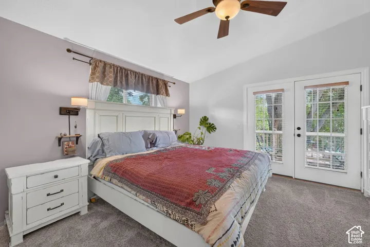 Vaulted ceiling with a ceiling fan, plush carpet flooring, and double glass-paneled doors with internal blinds
