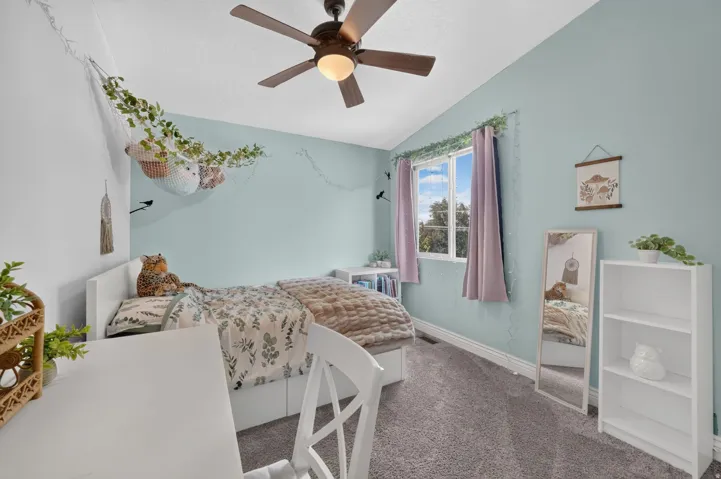 Ceiling fan with integrated light fixture, window with natural light, wall-to-wall carpeting, built-in shelving, and white baseboards