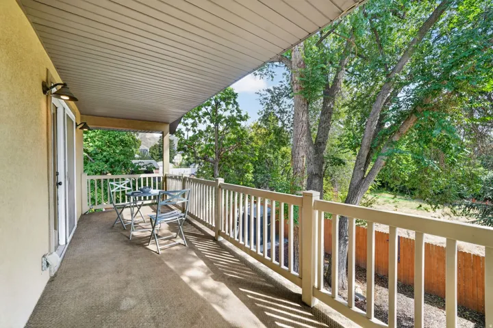 Covered outdoor balcony with a light-colored stucco exterior, sliding glass door, and a white railing