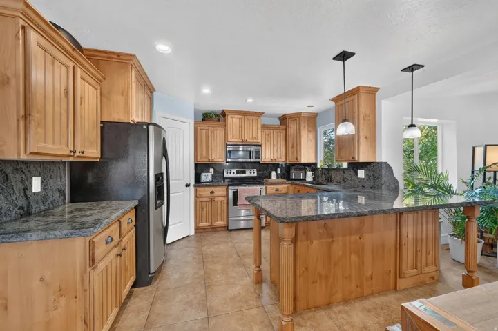 Kitchen featuring wood-finish cabinetry, granite countertops, stainless steel appliances, a center island with pendant lighting, and tiled flooring