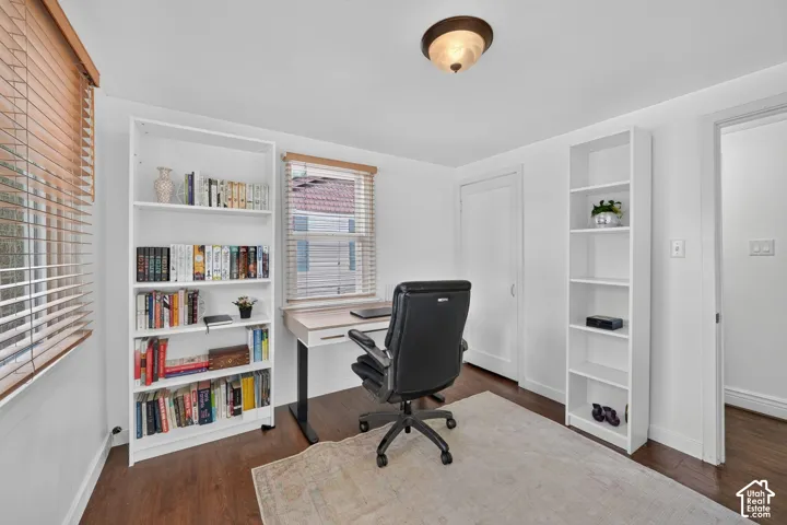 Rich wood-finish flooring, bright white walls, two windows with wood blinds, and a semi-flush mount ceiling fixture
