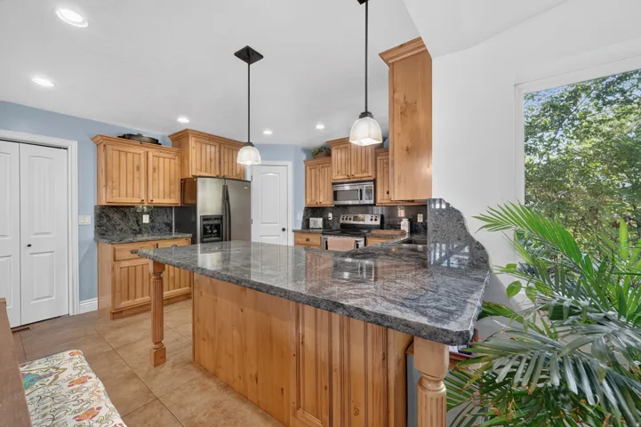 Kitchen featuring a large island with stone countertop, wood cabinetry, stainless steel appliances, and pendant lighting