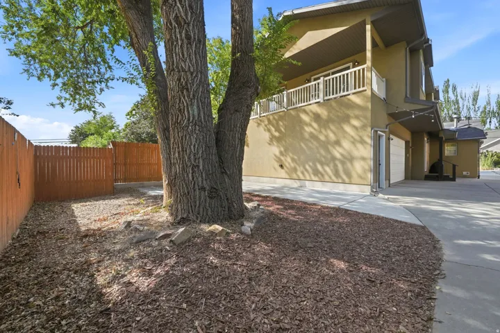 Mature tree with ground cover, wood privacy fencing, stucco exterior, upper-level balcony, and an attached garage