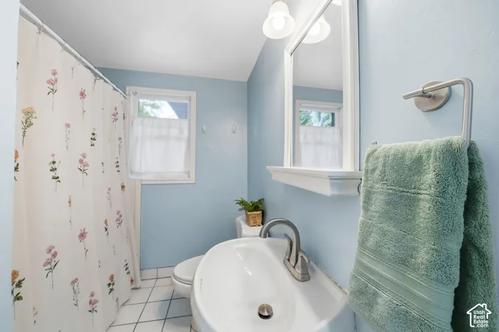 Recessed window with white trim, ceramic tile flooring, pedestal sink with single-handle faucet, wall-mounted mirror with integrated shelf, and brushed nickel towel bar