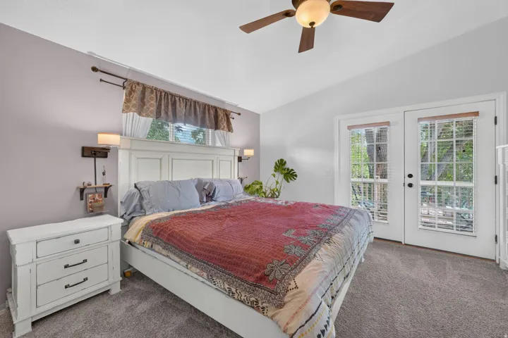 Vaulted ceiling with a ceiling fan, plush carpet flooring, and double glass-paneled doors with internal blinds