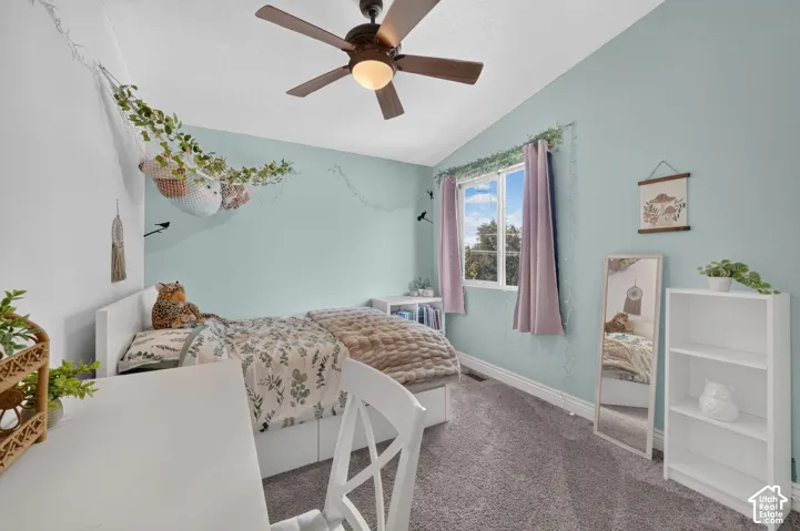 Ceiling fan with integrated light fixture, window with natural light, wall-to-wall carpeting, built-in shelving, and white baseboards