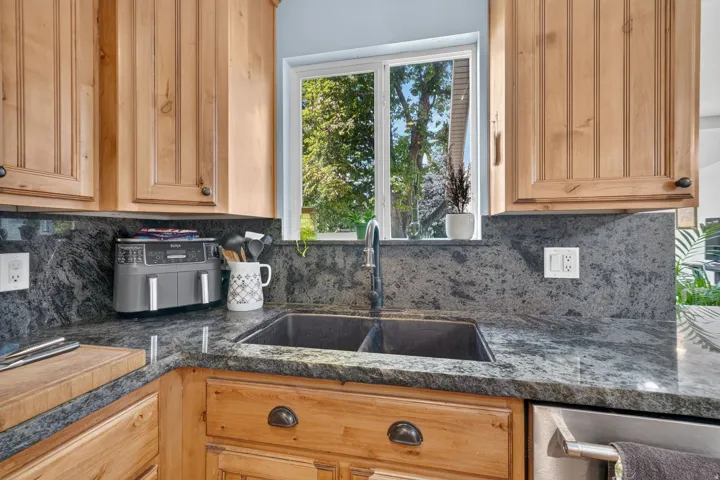Kitchen featuring wood cabinetry, dark stone countertops, a double basin sink with a gooseneck faucet, and a window