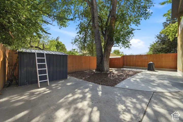 Private yard featuring a wood privacy fence, a mature shade tree, a concrete patio, and a storage shed with a metal roof