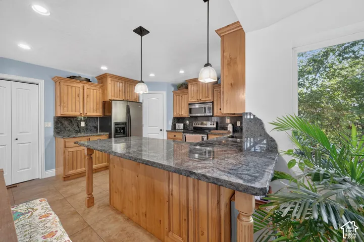 Kitchen featuring a large island with stone countertop, wood cabinetry, stainless steel appliances, and pendant lighting
